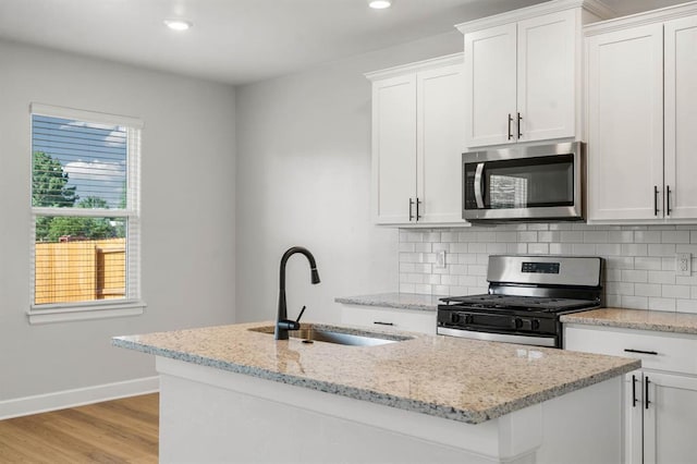 kitchen featuring backsplash, appliances with stainless steel finishes, a center island with sink, a sink, and baseboards