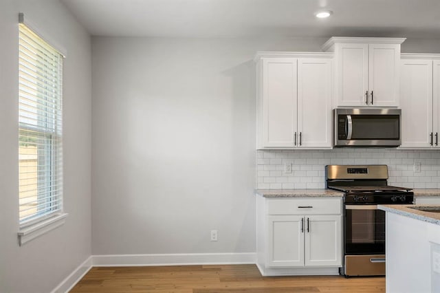 kitchen with white cabinets, appliances with stainless steel finishes, light stone counters, decorative backsplash, and light wood-type flooring