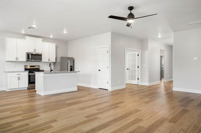 kitchen with open floor plan, ceiling fan, light wood-type flooring, backsplash, and stainless steel appliances