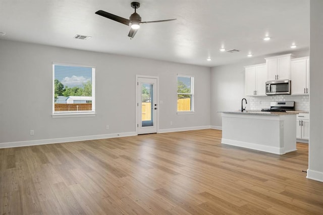 unfurnished living room with ceiling fan, visible vents, a sink, and light wood-style floors