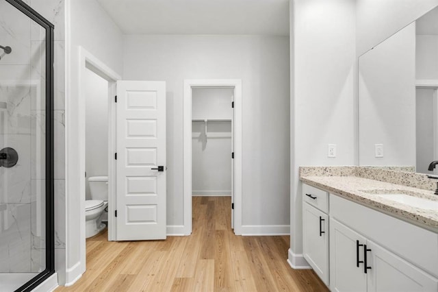 full bathroom with a walk in closet, a marble finish shower, and wood finished floors