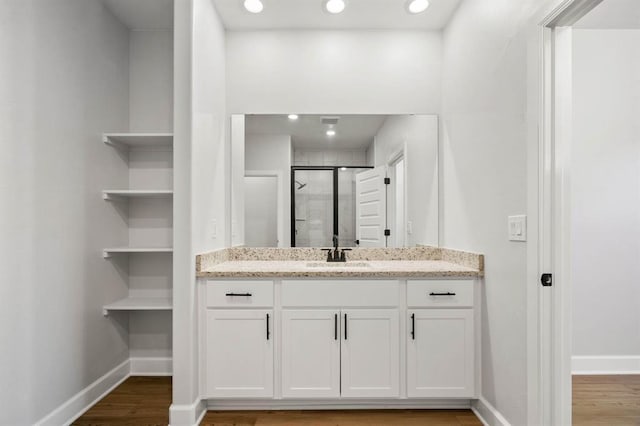 bathroom featuring vanity, baseboards, wood finished floors, and a stall shower
