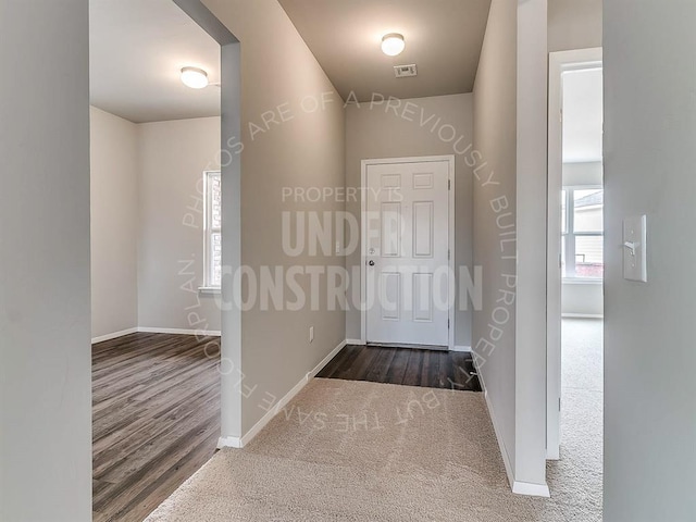 corridor featuring baseboards, dark wood finished floors, visible vents, and dark colored carpet