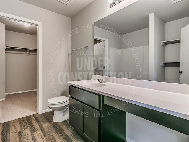 full bath featuring vanity, visible vents, wood finished floors, toilet, and a walk in closet