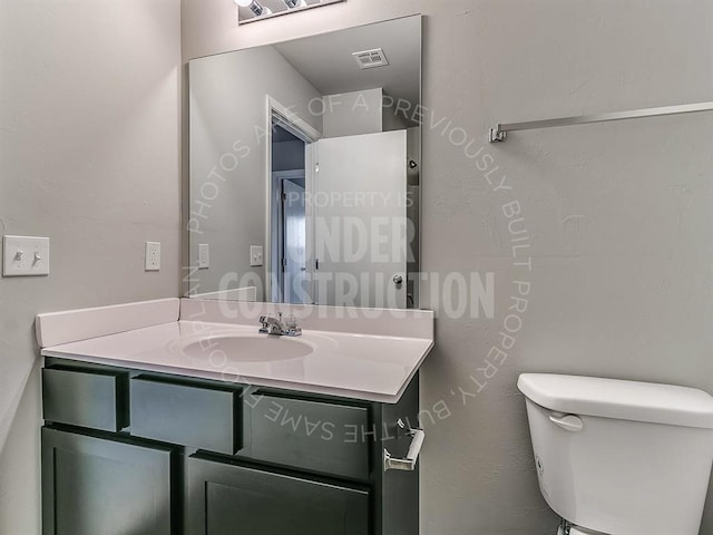 half bath featuring visible vents, toilet, and vanity
