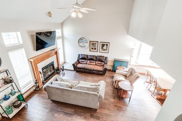 living area with a ceiling fan, a glass covered fireplace, wood finished floors, and high vaulted ceiling