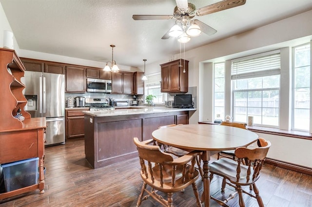 kitchen with a peninsula, ceiling fan, dark wood finished floors, appliances with stainless steel finishes, and decorative light fixtures