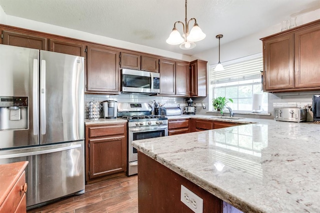kitchen featuring decorative light fixtures, appliances with stainless steel finishes, tasteful backsplash, wood finished floors, and a notable chandelier