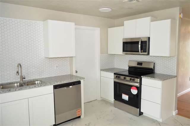kitchen with a sink, appliances with stainless steel finishes, light stone countertops, and white cabinetry
