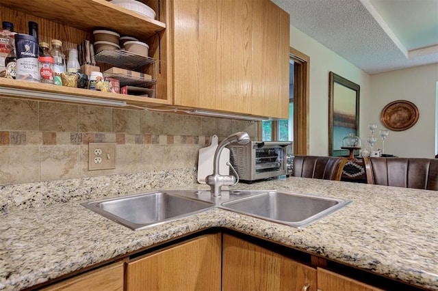 kitchen with a textured ceiling, open shelves, a sink, and tasteful backsplash