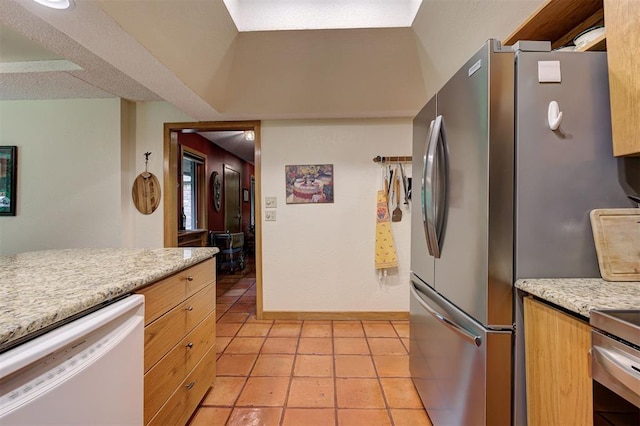 kitchen with baseboards, freestanding refrigerator, light tile patterned floors, and dishwasher