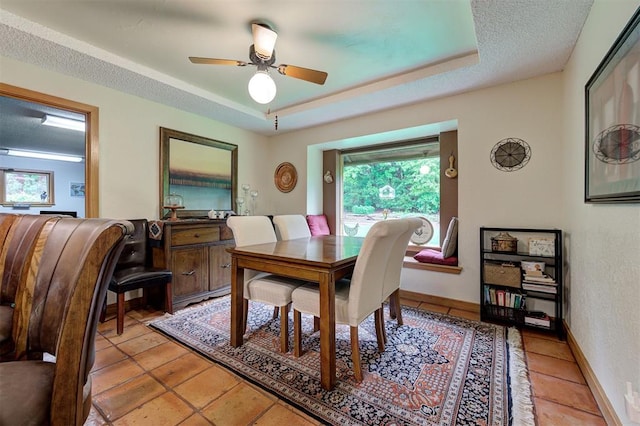 dining space with light tile patterned floors, a ceiling fan, a tray ceiling, and a wealth of natural light