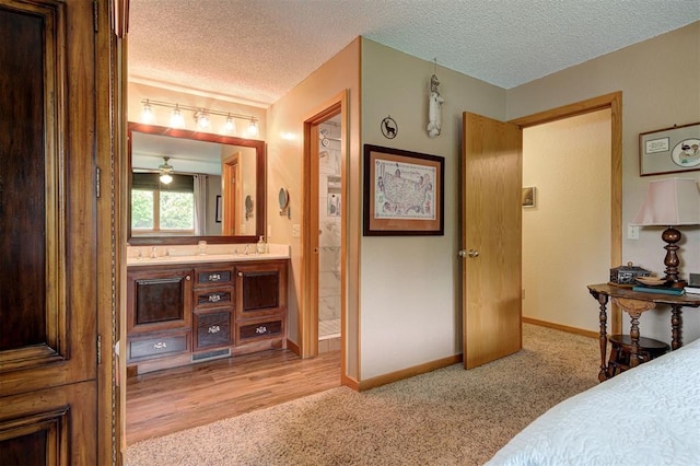 bedroom with a textured ceiling, light colored carpet, baseboards, and ensuite bath