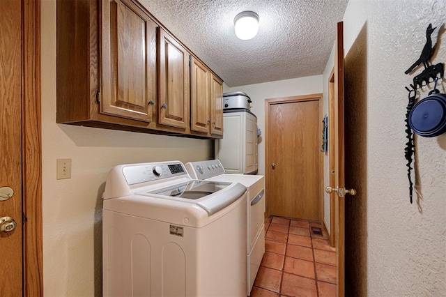 laundry room with a textured ceiling, washing machine and clothes dryer, cabinet space, light tile patterned floors, and a textured wall