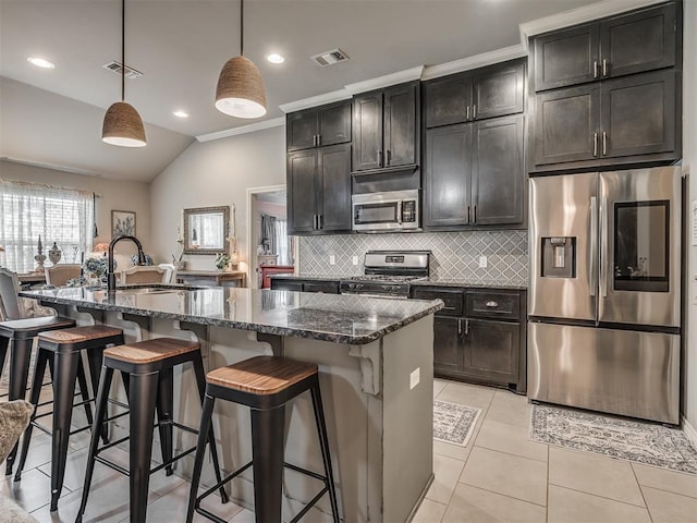 kitchen with decorative backsplash, appliances with stainless steel finishes, a sink, dark stone countertops, and an island with sink