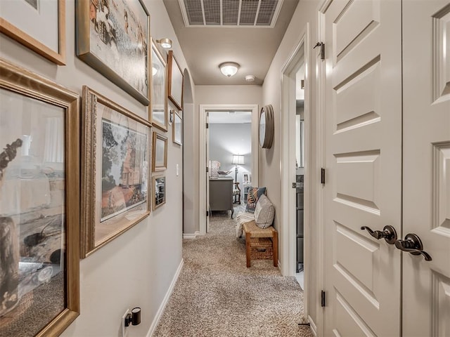corridor with baseboards, visible vents, and light carpet