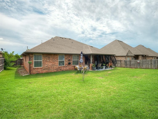 rear view of house featuring a yard, brick siding, a fenced backyard, and roof with shingles