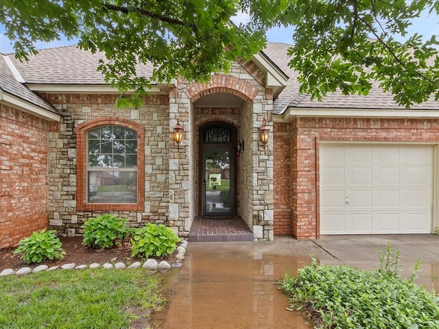 entrance to property with roof with shingles, stone siding, an attached garage, and brick siding