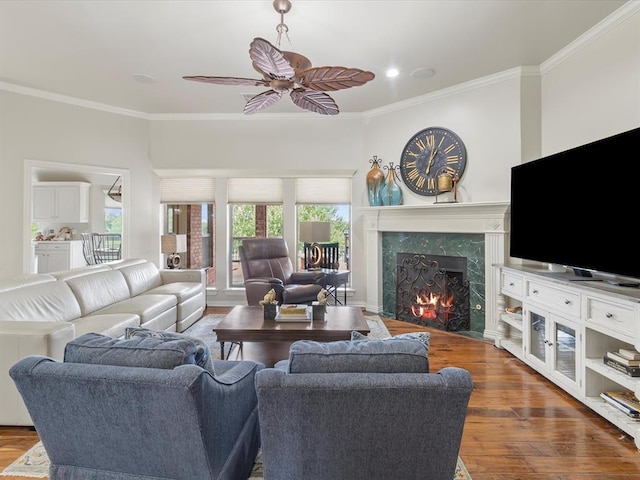living room featuring crown molding, a high end fireplace, wood finished floors, and ceiling fan