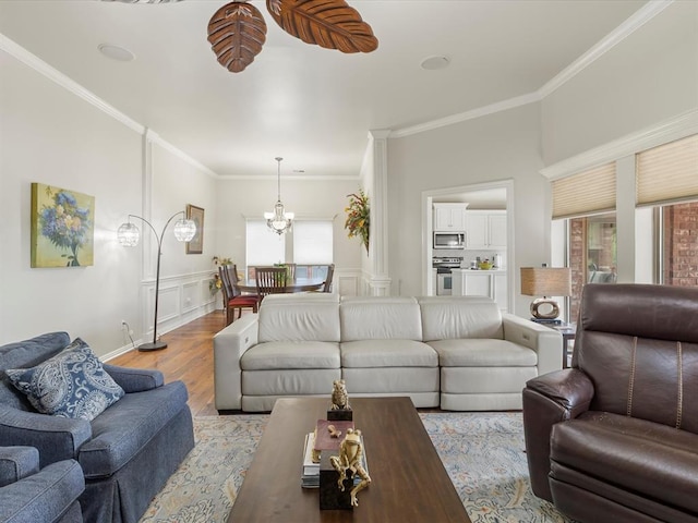 living room with wood finished floors, ornamental molding, a chandelier, and wainscoting