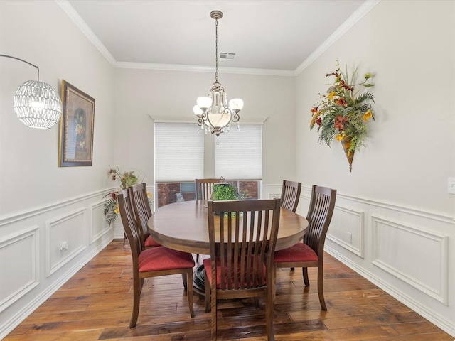 dining area featuring a chandelier, wood-type flooring, crown molding, a decorative wall, and a wainscoted wall