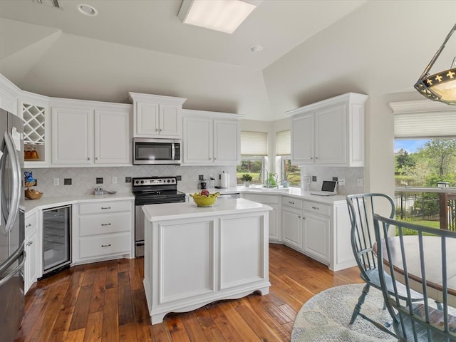 kitchen with appliances with stainless steel finishes, wine cooler, white cabinets, light countertops, and tasteful backsplash