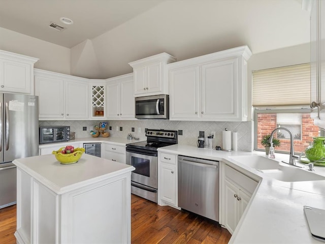 kitchen with appliances with stainless steel finishes, a sink, wine cooler, white cabinetry, and vaulted ceiling