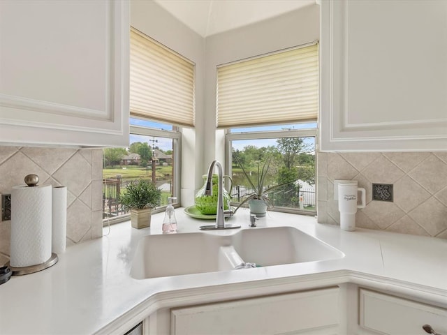 kitchen view of a sink, light countertops, decorative backsplash, and white cabinets