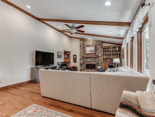 living room with ceiling fan, a fireplace, light wood-style flooring, baseboards, and vaulted ceiling with beams