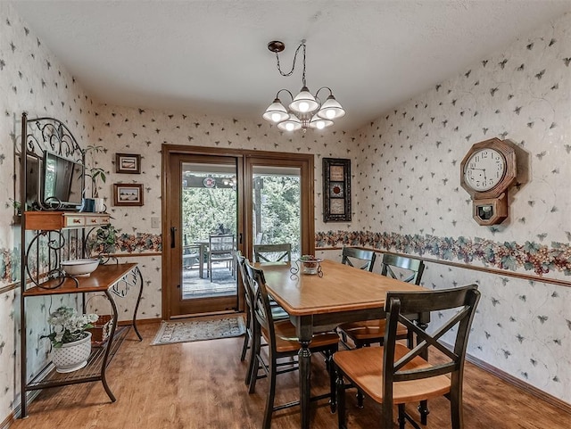 dining area with baseboards, wallpapered walls, wood finished floors, and a chandelier