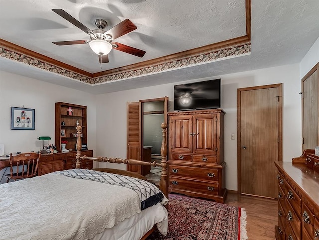 bedroom with a raised ceiling, ceiling fan, a textured ceiling, and light wood-style flooring
