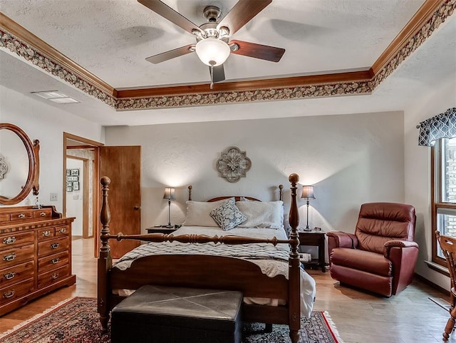 bedroom with visible vents, crown molding, light wood-style floors, a textured ceiling, and a tray ceiling