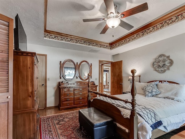 bedroom with a textured ceiling, visible vents, wood finished floors, baseboards, and a tray ceiling