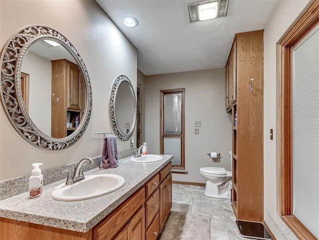bathroom featuring a sink, baseboards, toilet, and double vanity