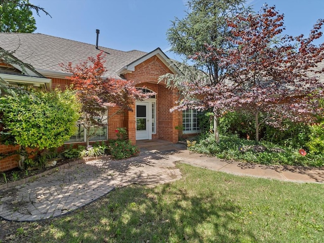 view of front of home featuring brick siding, a shingled roof, and a front yard