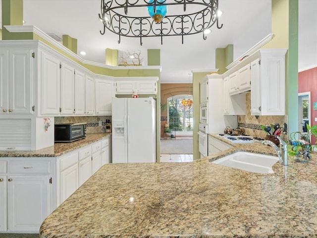 kitchen featuring white appliances, backsplash, light stone countertops, and a sink