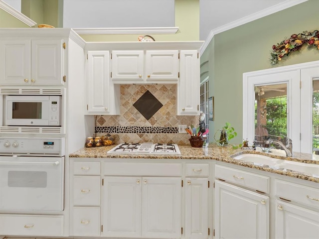 kitchen featuring light stone countertops, a sink, white appliances, white cabinetry, and backsplash