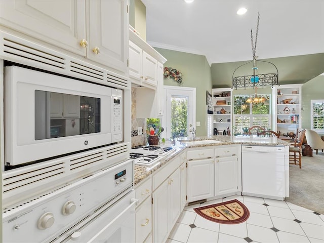 kitchen featuring a peninsula, white appliances, white cabinets, a sink, and a notable chandelier