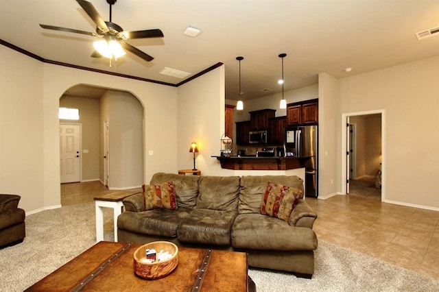 living room featuring arched walkways, ceiling fan, baseboards, light carpet, and crown molding