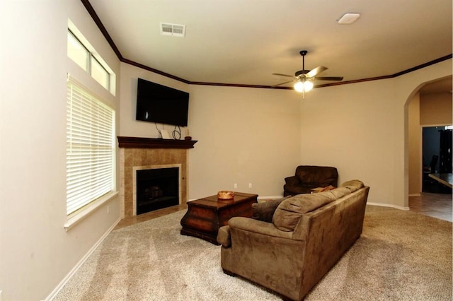living area with arched walkways, carpet, ornamental molding, a ceiling fan, and a fireplace
