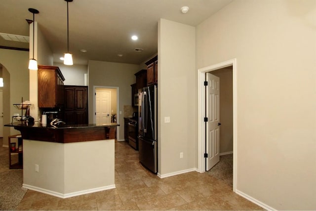 kitchen featuring freestanding refrigerator, dark countertops, a peninsula, arched walkways, and hanging light fixtures