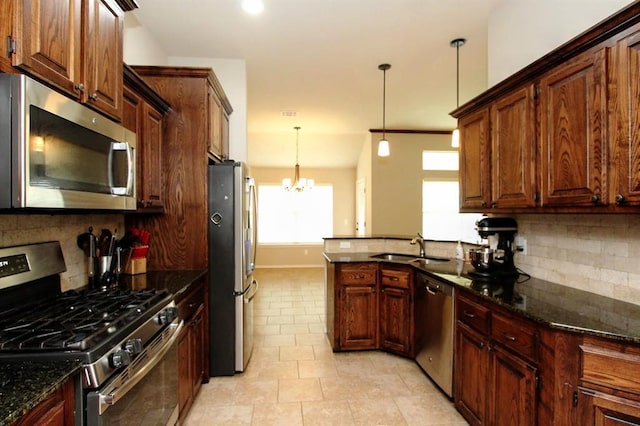 kitchen with appliances with stainless steel finishes, a peninsula, tasteful backsplash, a sink, and dark stone countertops
