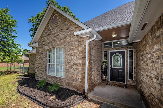 property entrance with roof with shingles, fence, and brick siding