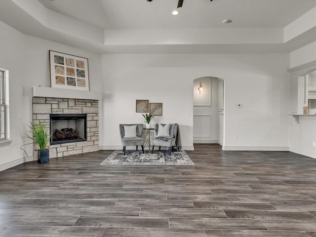 living area with arched walkways, a fireplace, wood finished floors, a tray ceiling, and recessed lighting