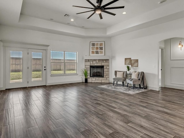 living area with a raised ceiling, ceiling fan, arched walkways, and wood finished floors