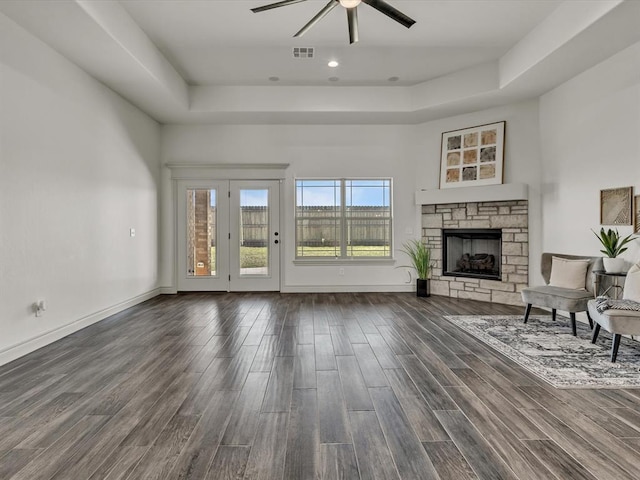 unfurnished living room featuring dark wood finished floors, a stone fireplace, a ceiling fan, a tray ceiling, and visible vents