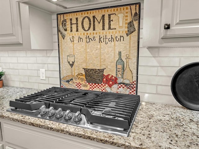 room details with stainless steel gas cooktop, white cabinets, light stone countertops, and tasteful backsplash