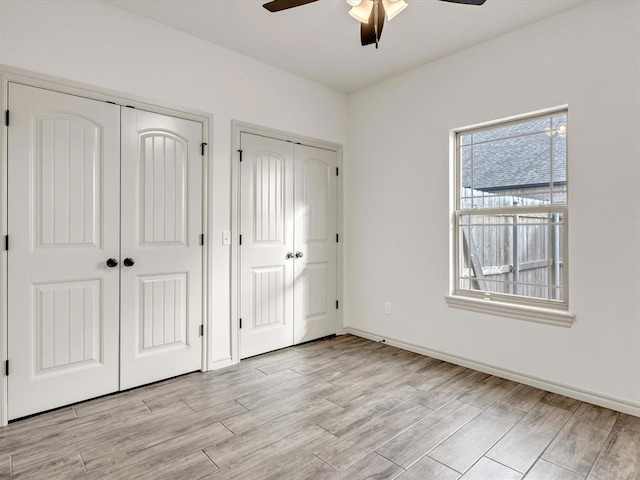 unfurnished bedroom featuring light wood-style floors, multiple closets, ceiling fan, and baseboards