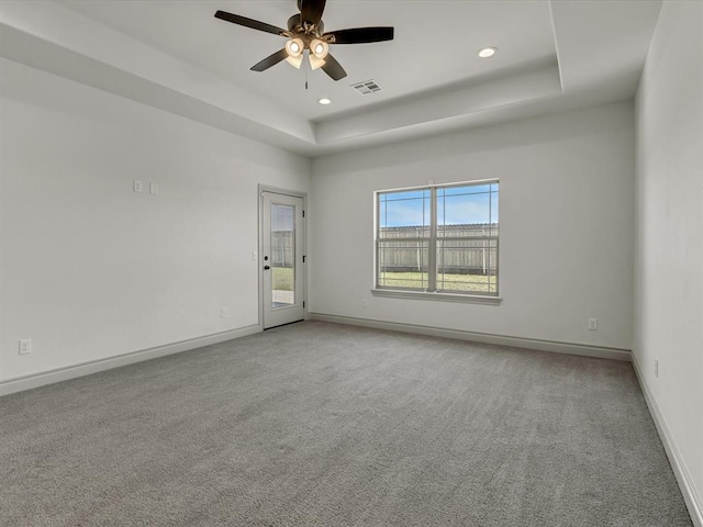 carpeted spare room featuring visible vents, baseboards, recessed lighting, a tray ceiling, and a ceiling fan