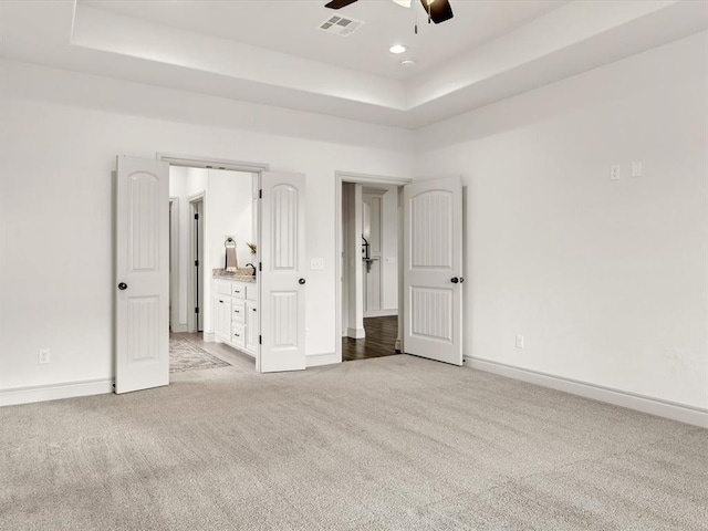 unfurnished bedroom with a tray ceiling, light colored carpet, baseboards, and visible vents